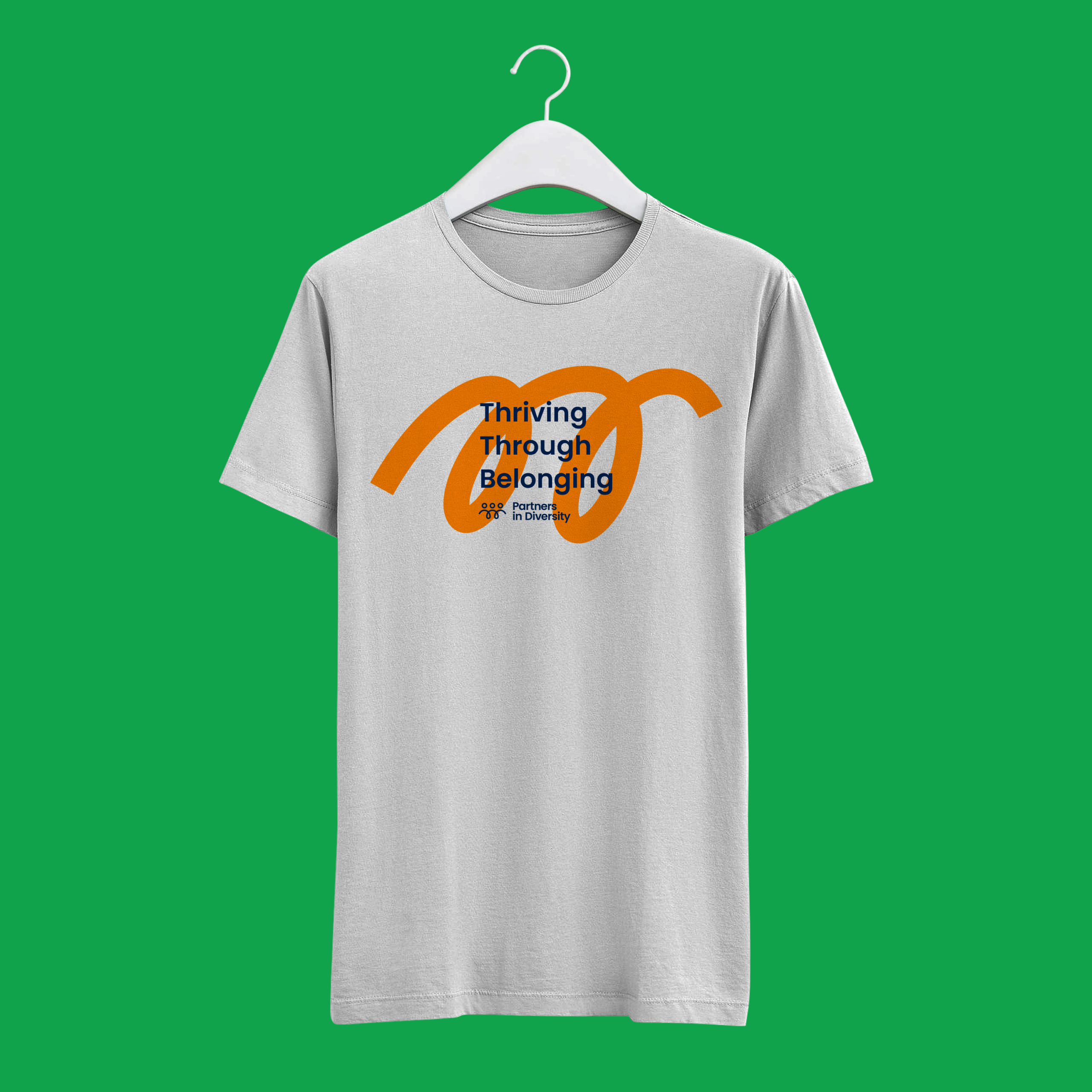A white t-shirt on a hanger features an orange abstract design and the text “Thriving Through Belonging” plus smaller text, against a bright green background.