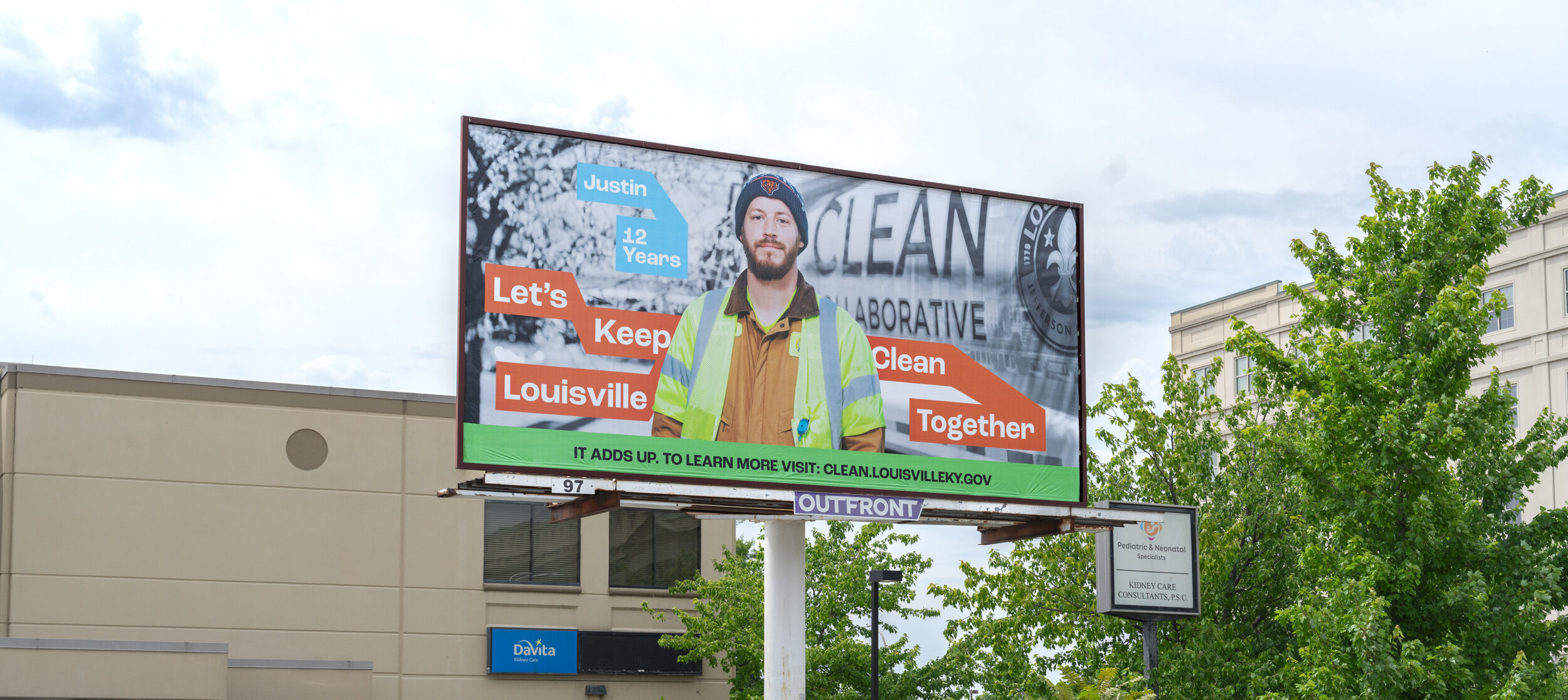 A billboard in a parking lot features a man in a yellow jacket and beanie with text: “Justin, 12 years. Let’s Keep Louisville Clean Together.” Several parked cars and trees surround the scene.