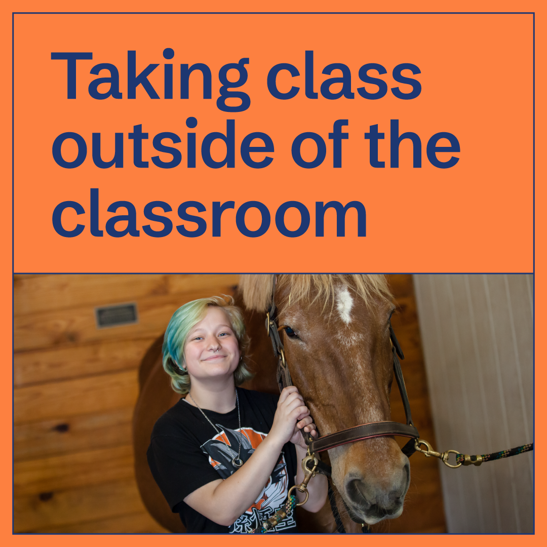 A smiling student with short, light blue-green hair stands next to a brown horse inside a wooden stable. Bold text above reads, Taking class outside of the classroom.