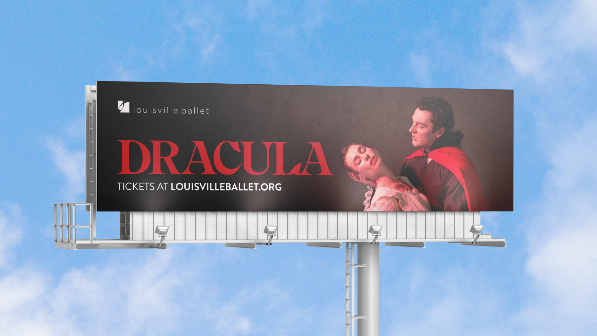 A billboard for Louisville Ballet’s Dracula shows a man in a red cape holding a woman in white with her head tilted back. Text reads: “DRACULA. Tickets at LOUISVILLEBALLET.ORG” against a dark background.