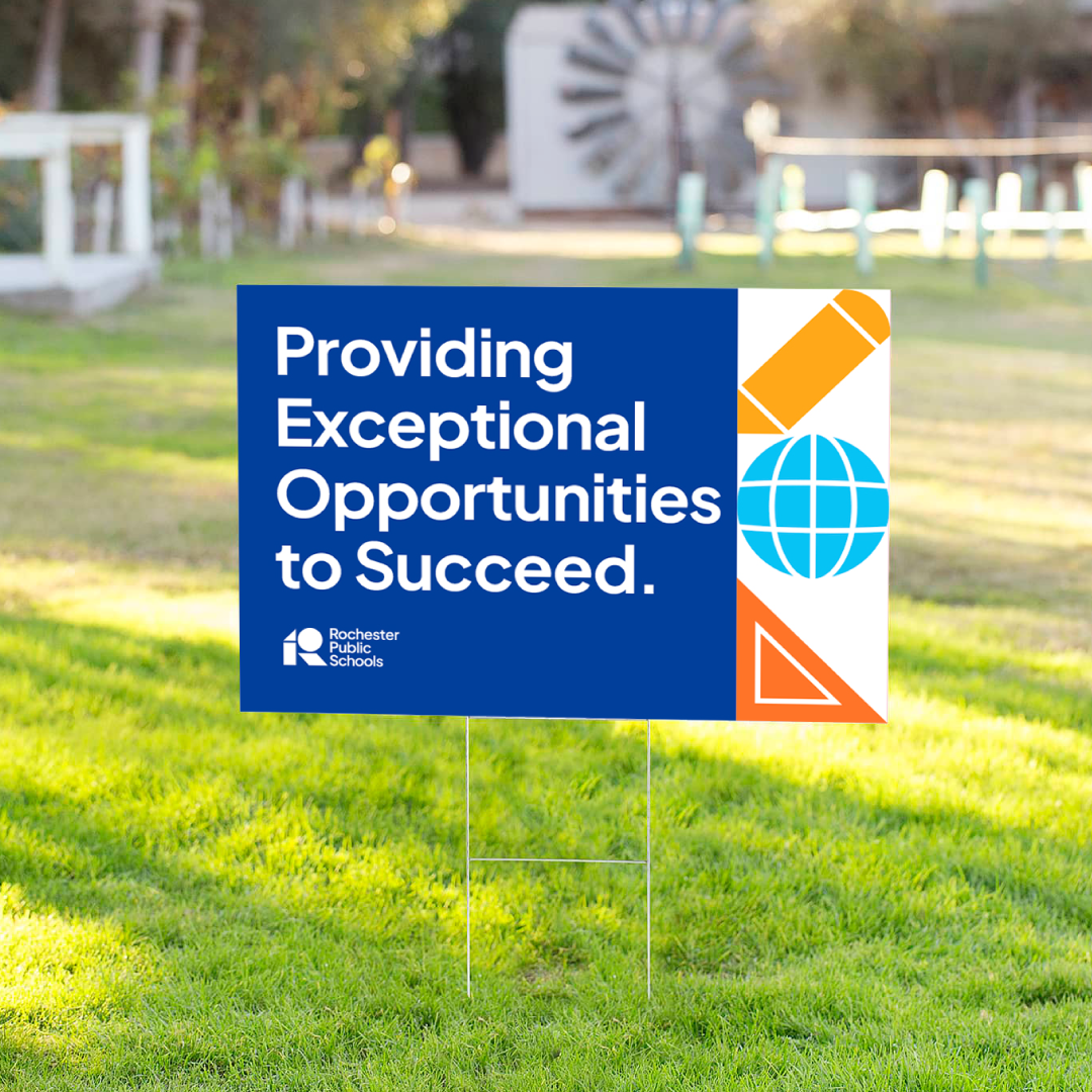 A Rochester Public Schools yard sign on a lawn that reads, Providing Exceptional Opportunities to Succeed, with icons of a pencil, a globe, and a triangle.